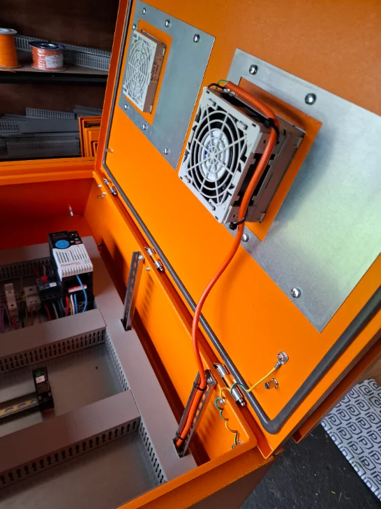 Switchboard door internal during build — cooling fan cutouts and earth bonding strap