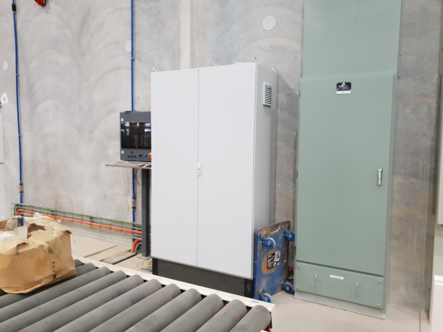 New process-line switchboard installed alongside the existing painted MCC, conveyor running in the foreground