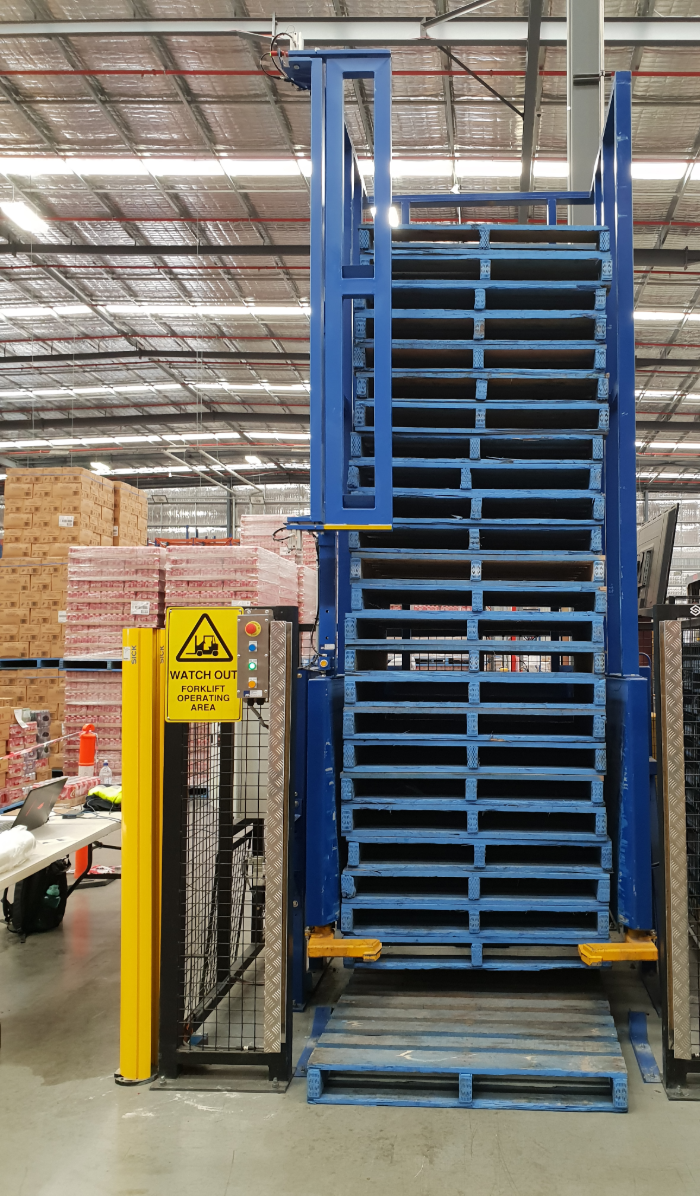 Tall vertical pallet dispenser with stacked CHEP pallets, SICK safety light curtain on the left and a yellow forklift warning sign on the door